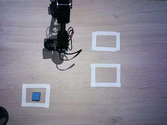Overhead bench camera: an Ohm Lab robot arm above a desk with the blue block placed inside the destination square